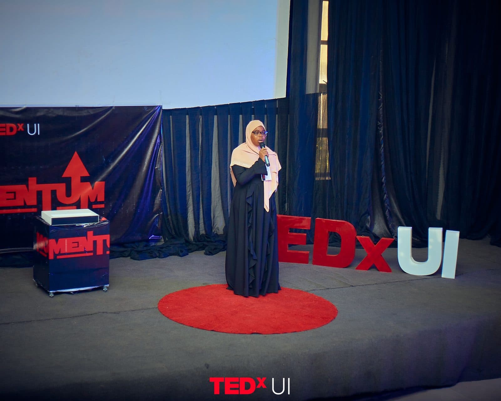 A speaker standing on the red dot beside the large TEDxUI stage letters.